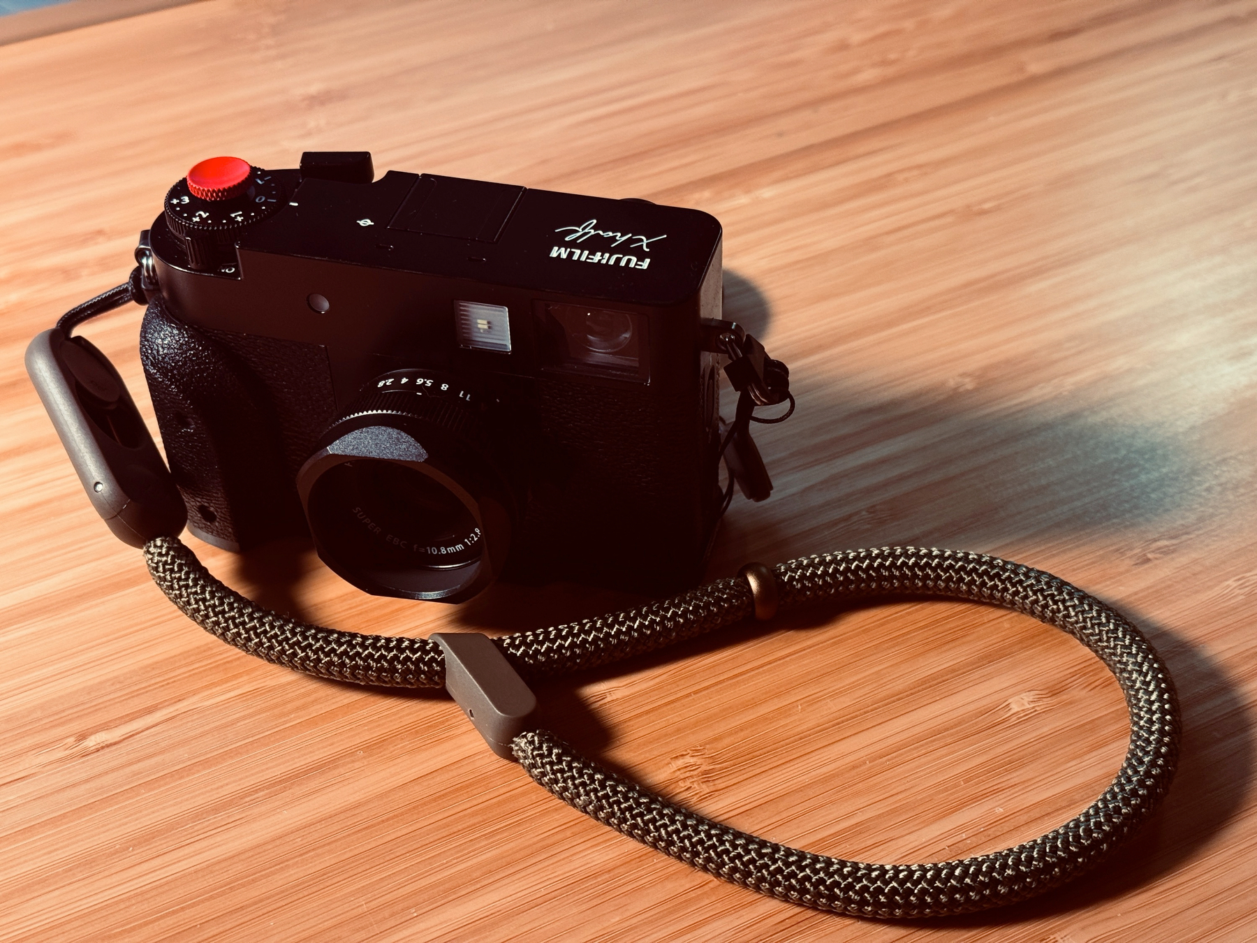 A Fujifilm X half with a rope wrist strap on a wooden surface.
